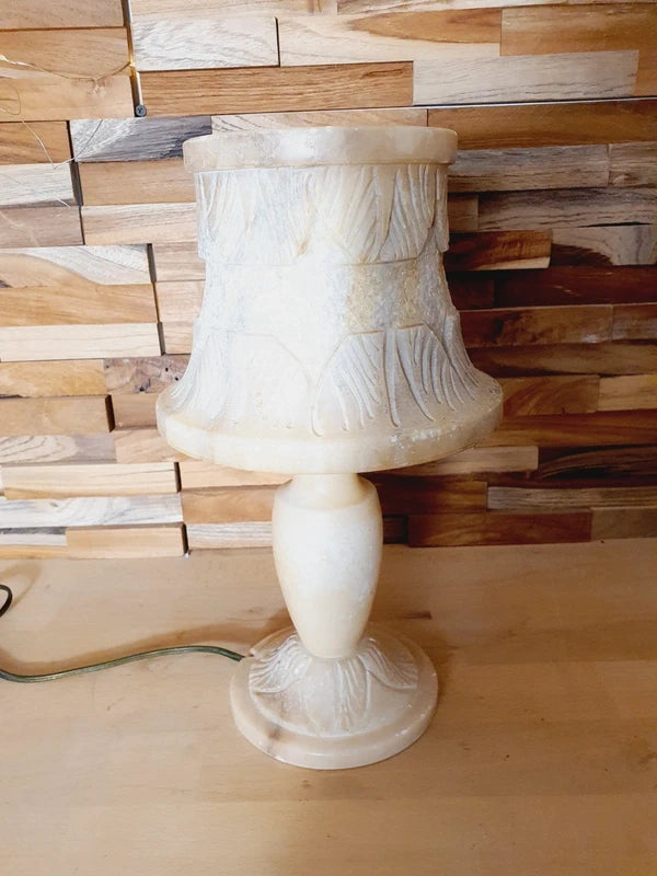 Lampe à poser italienne en albâtre de Volterra éteinte, posée sur un meuble en bois devant un mur de parement en bois. Pierre blanche et poreuse, créant une atmosphère cosy chic et chaleureuse.