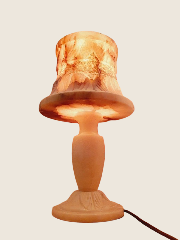 Lampe vintage en albâtre massif sculpté de 33 cm, style Hollywood Regency des années 60. sur fond neutre beige montrant le pied balustre et l'abat-jour minéral translucide illuminé d'une lumière chaude orangée.