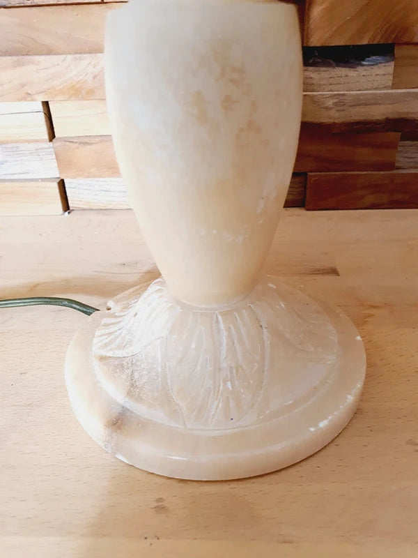 Lampe à poser italienne en albâtre de Volterra éteinte, posée sur un meuble en bois devant un mur de parement en bois. Pierre blanche et poreuse, créant une atmosphère cosy chic et chaleureuse.