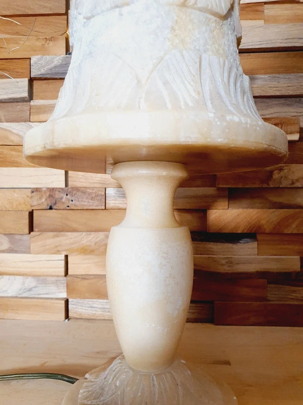 Lampe à poser italienne en albâtre de Volterra éteinte, posée sur un meuble en bois devant un mur de parement en bois. Pierre blanche et poreuse, créant une atmosphère cosy chic et chaleureuse.
