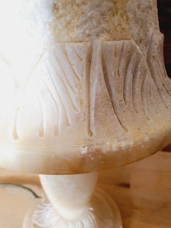 Lampe à poser italienne en albâtre de Volterra éteinte, posée sur un meuble en bois devant un mur de parement en bois. Pierre blanche et poreuse, créant une atmosphère cosy chic et chaleureuse.