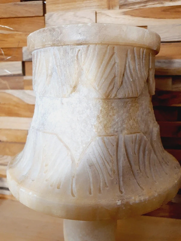 Lampe à poser italienne en albâtre de Volterra éteinte, posée sur un meuble en bois devant un mur de parement en bois. Pierre blanche et poreuse, créant une atmosphère cosy chic et chaleureuse.