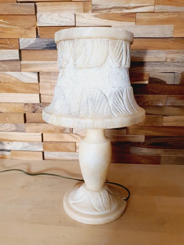 Lampe à poser italienne en albâtre de Volterra éteinte, posée sur un meuble en bois devant un mur de parement en bois. Pierre blanche et poreuse, créant une atmosphère cosy chic et chaleureuse.