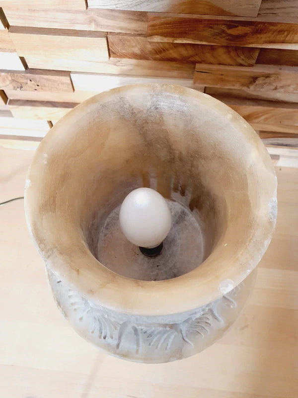 Lampe à poser italienne en albâtre de Volterra éteinte, posée sur un meuble en bois devant un mur de parement en bois. Pierre blanche et poreuse, créant une atmosphère cosy chic et chaleureuse.