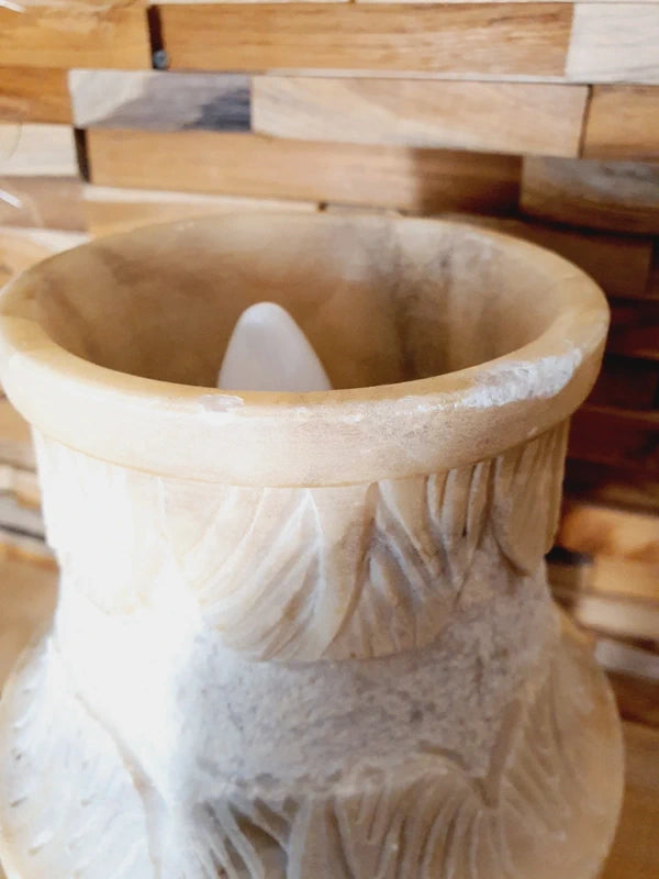 Lampe à poser italienne en albâtre de Volterra éteinte, posée sur un meuble en bois devant un mur de parement en bois. Pierre blanche et poreuse, créant une atmosphère cosy chic et chaleureuse.