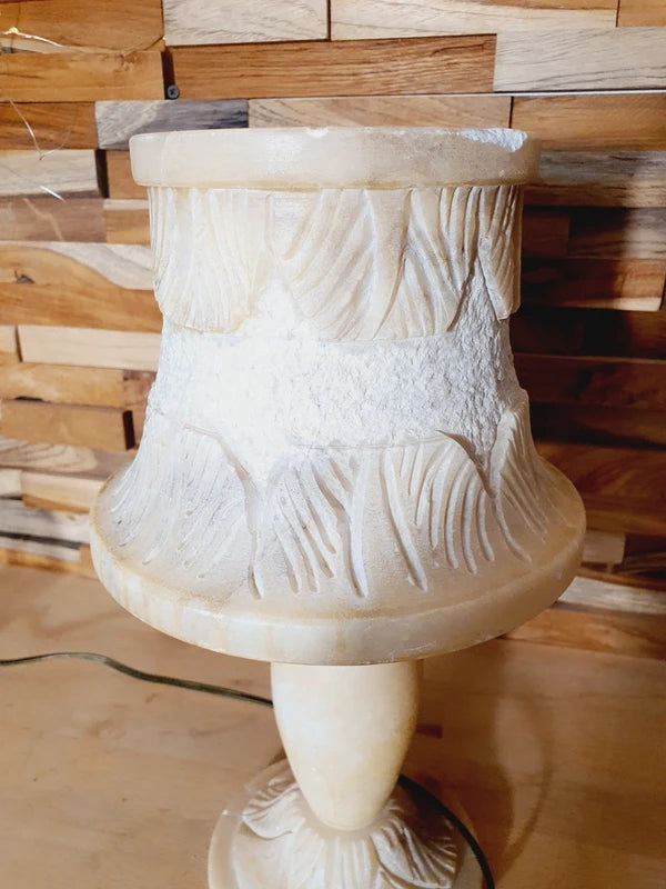 Lampe à poser italienne en albâtre de Volterra éteinte, posée sur un meuble en bois devant un mur de parement en bois. Pierre blanche et poreuse, créant une atmosphère cosy chic et chaleureuse.