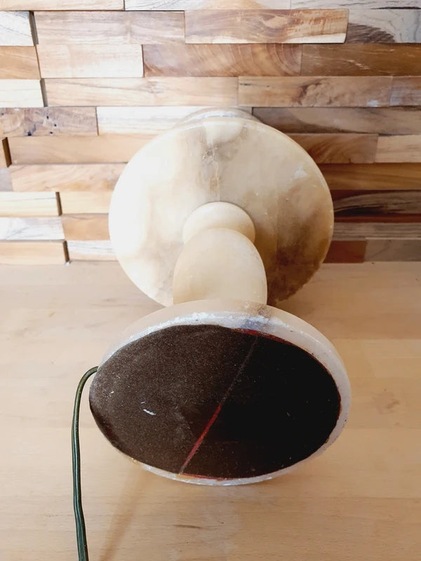 Lampe à poser italienne en albâtre de Volterra éteinte, posée sur un meuble en bois devant un mur de parement en bois. Pierre blanche et poreuse, créant une atmosphère cosy chic et chaleureuse.