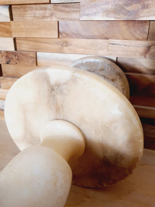 Lampe à poser italienne en albâtre de Volterra éteinte, posée sur un meuble en bois devant un mur de parement en bois. Pierre blanche et poreuse, créant une atmosphère cosy chic et chaleureuse.