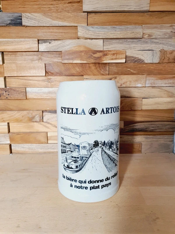 Grande choppe à bière en grès beige portant le logo Stella Artois et l'inscription noire "la bière qui donne du relief à notre plat pays" avec une illustration de péniche.