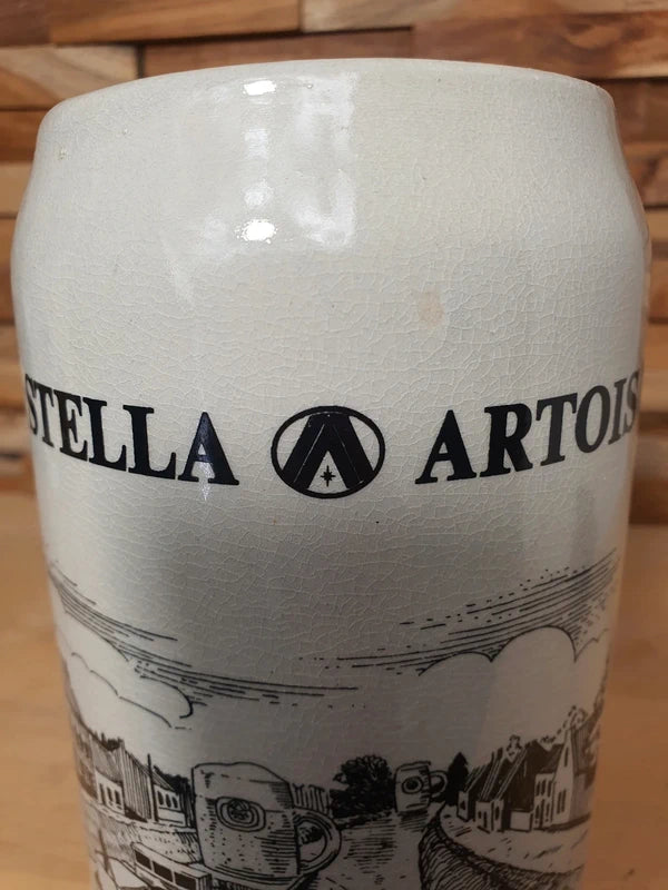Grande choppe à bière en grès beige portant le logo Stella Artois et l'inscription noire "la bière qui donne du relief à notre plat pays" avec une illustration de péniche.