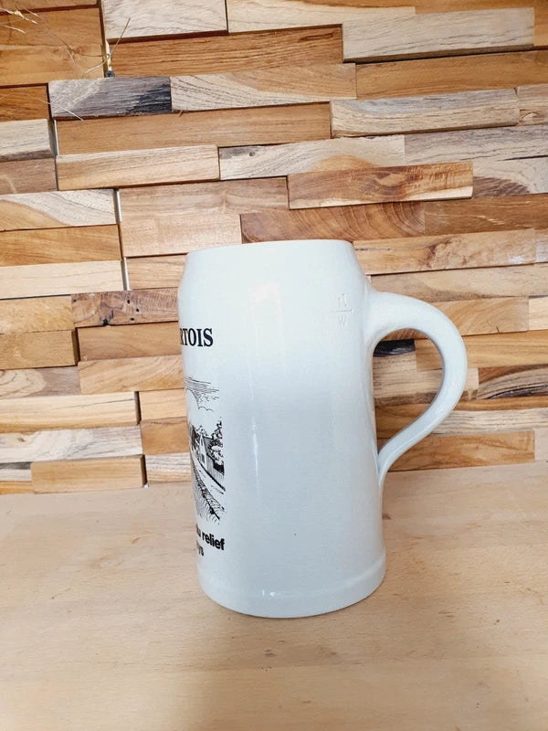 Grande choppe à bière en grès beige portant le logo Stella Artois et l'inscription noire "la bière qui donne du relief à notre plat pays" avec une illustration de péniche.