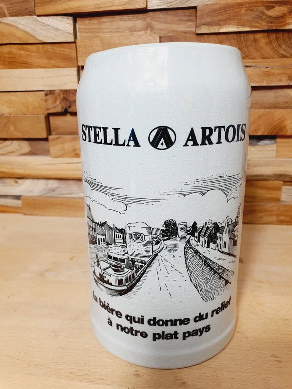Grande choppe à bière en grès beige portant le logo Stella Artois et l'inscription noire "la bière qui donne du relief à notre plat pays" avec une illustration de péniche.