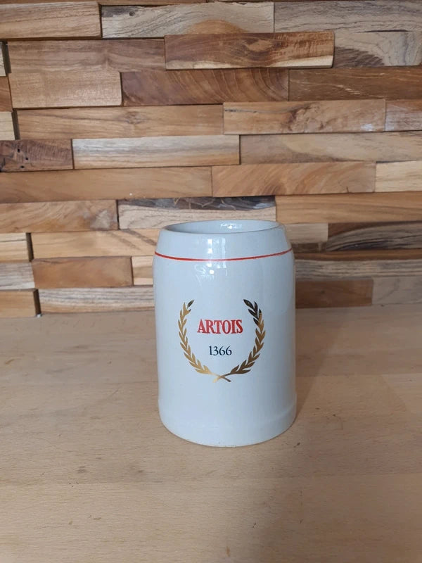 Petite choppe à bière vintage Stella Artois en grès gris avec logo rouge et or, format 25 cl, posée sur un fond en bois.