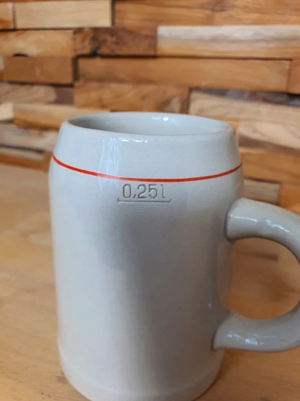 Petite choppe à bière vintage Stella Artois en grès gris avec logo rouge et or, format 25 cl, posée sur un fond en bois.