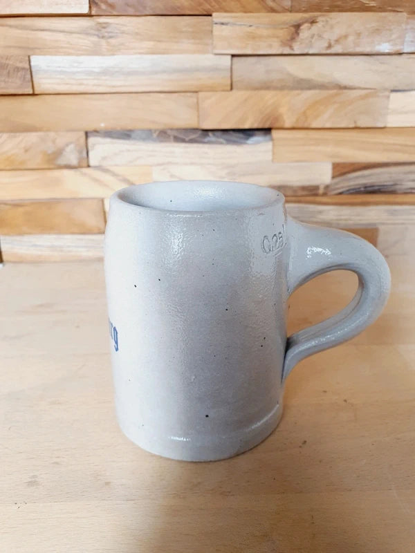 Petite choppe à bière en grès gris et bleu cobalt avec logo Kronenbourg en relief, fabriquée en Allemagne, style traditionnel rustique.