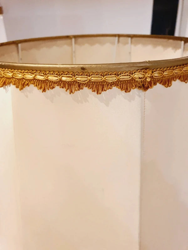 Lampe de table de style Regency & Art Français années 50-60. Hauteur 55,5 cm. Elle possède un pied en laiton sculpté combinant une base ornée. Son grand abat-jour en tissu de couleur crème est bordé de galons décoratifs. 