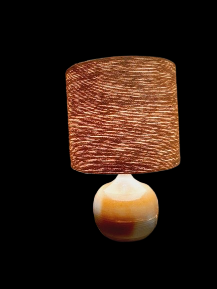 Une lampe vintage imposante composée d'un pied en grès français beige moucheté et d'un grand abat-jour en toile de jute tressée, diffusant une lumière chaude dans un intérieur à la décoration naturelle.