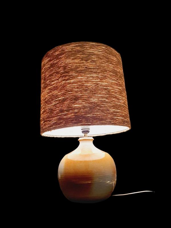Une lampe vintage imposante composée d'un pied en grès français beige moucheté et d'un grand abat-jour en toile de jute tressée, diffusant une lumière chaude dans un intérieur à la décoration naturelle.