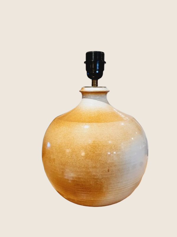 Une lampe vintage imposante composée d'un pied en grès français beige moucheté et d'un grand abat-jour en toile de jute tressée, diffusant une lumière chaude dans un intérieur à la décoration naturelle.