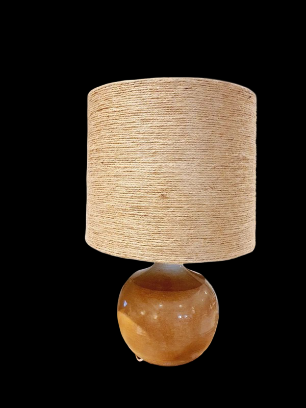 Une lampe vintage imposante composée d'un pied en grès français beige moucheté et d'un grand abat-jour en toile de jute tressée, diffusant une lumière chaude dans un intérieur à la décoration naturelle.