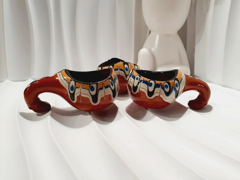 Lot de 3 mini choppes coupelles asymétriques avec anse en crochet en céramique vernissée traditionnelle de Troyan des années 1970 avec le motif œil de paon bulgare fait main aux nuances ocre, blanche, bleue et noire, montrant les dessous en argile rouge terre cuite propre.