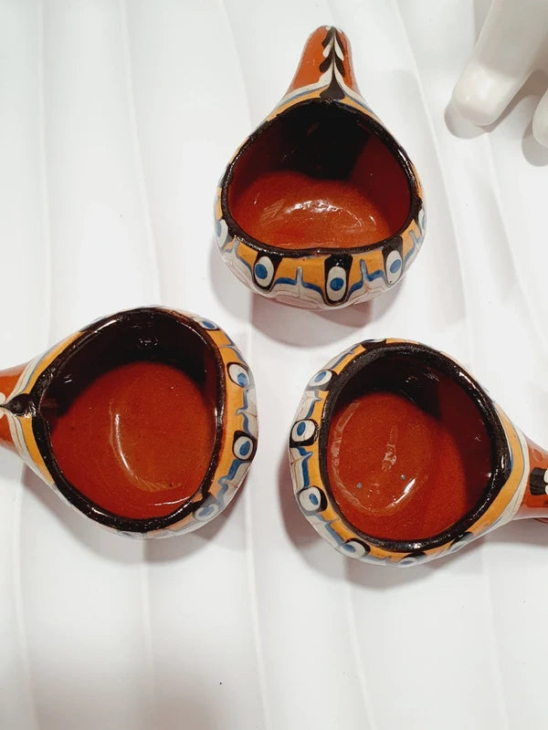 Lot de 3 mini choppes coupelles asymétriques avec anse en crochet en céramique vernissée traditionnelle de Troyan des années 1970 avec le motif œil de paon bulgare fait main aux nuances ocre, blanche, bleue et noire, montrant les dessous en argile rouge terre cuite propre.