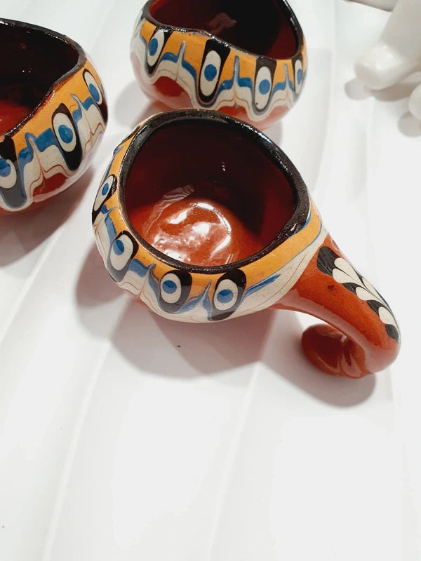 Lot de 3 mini choppes coupelles asymétriques avec anse en crochet en céramique vernissée traditionnelle de Troyan des années 1970 avec le motif œil de paon bulgare fait main aux nuances ocre, blanche, bleue et noire, montrant les dessous en argile rouge terre cuite propre.