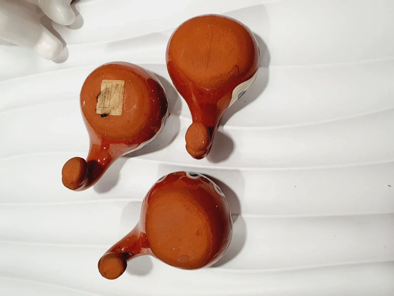 Lot de 3 mini choppes coupelles asymétriques avec anse en crochet en céramique vernissée traditionnelle de Troyan des années 1970 avec le motif œil de paon bulgare fait main aux nuances ocre, blanche, bleue et noire, montrant les dessous en argile rouge terre cuite propre.