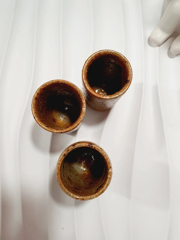 Lot de 3 petits gobelets cylindriques en grès pyrité vintage fait main des années 1970 aux nuances ocres et brunes mouchetées avec une finition vernissée brillante.