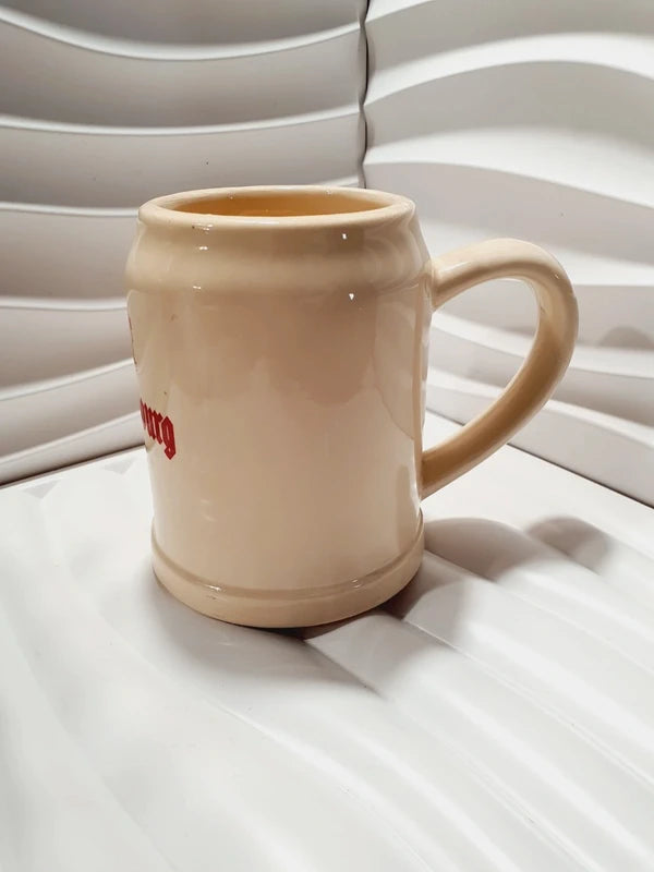 Chope à bière ancienne de marque Kronenbourg en céramique émaillée couleur crème et rouge en forme de tonneau publicitaire, inscription Baudour Belgium CRF sous le dessous, style bistrot vintage des années 1970 utilisé comme cache-pot décoratif pour plante verte.