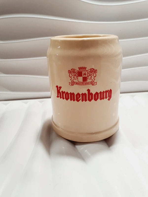 Chope à bière ancienne de marque Kronenbourg en céramique émaillée couleur crème et rouge en forme de tonneau publicitaire, inscription Baudour Belgium CRF sous le dessous, style bistrot vintage des années 1970 utilisé comme cache-pot décoratif pour plante verte.