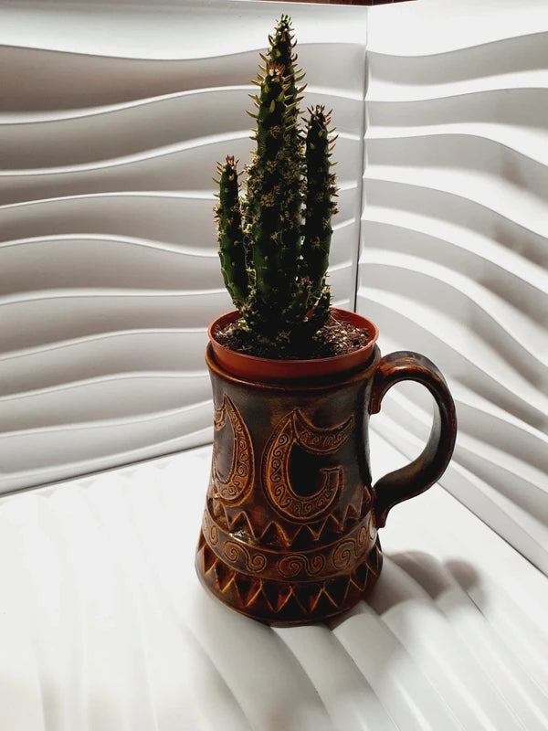 Grande chope en céramique d'art émaillée couleur marron avec motifs géométriques et volutes gravés en relief, signée Beny Leleu sous la base, style poterie artisanale des années 1970 utilisée comme cache-pot pour un cactus.