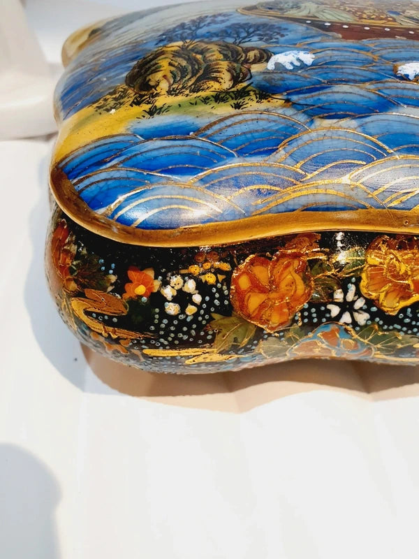 Boîte à bijoux rectangulaire festonnée en porcelaine vintage style Satsuma des années 1970 avec un couvercle illustré d'une scène traditionnelle de femmes et fillette sur une pirogue, richement décorée de fleurs colorées et de détails dorés à l'or fin, montrant le dessous estampillé d'une étiquette rouge Made in China Satsuma.