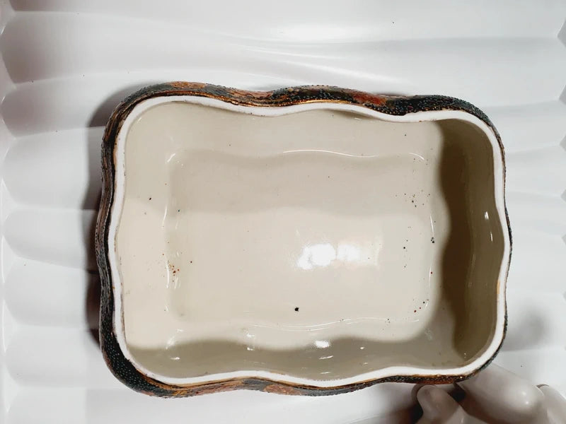 Boîte à bijoux rectangulaire festonnée en porcelaine vintage style Satsuma des années 1970 avec un couvercle illustré d'une scène traditionnelle de femmes et fillette sur une pirogue, richement décorée de fleurs colorées et de détails dorés à l'or fin, montrant le dessous estampillé d'une étiquette rouge Made in China Satsuma.