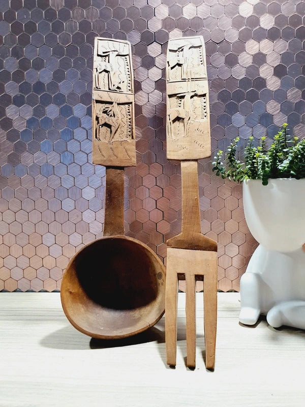 Ensemble de couverts à salade vintage en bois véritable sculpté à la main des années 1970 composé d'une grande fourchette trident et d'une cuillère louche, ornées de motifs de cerfs, biches et faons en relief sur le manche avec encoche repose-plat au dos, montrant un léger éclat de cuisson ou d'usage sur le rebord supérieur du buvant.