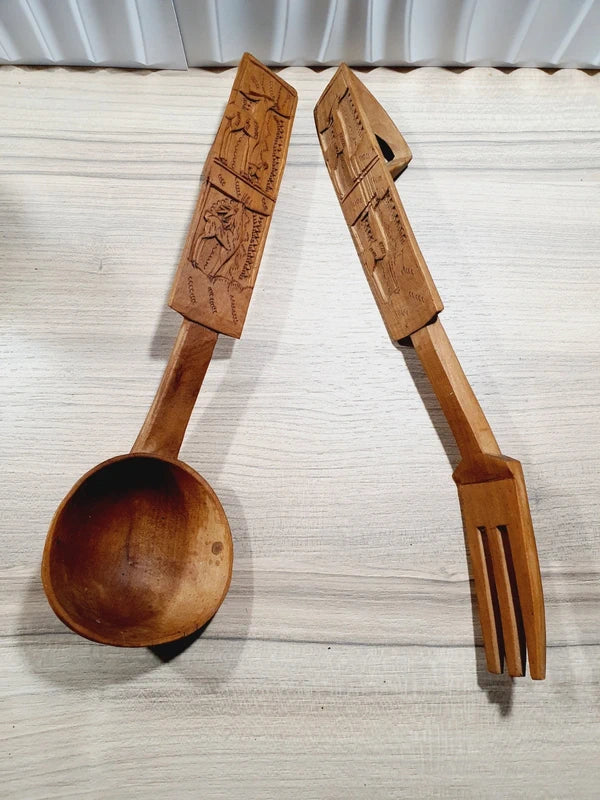 Ensemble de couverts à salade vintage en bois véritable sculpté à la main des années 1970 composé d'une grande fourchette trident et d'une cuillère louche, ornées de motifs de cerfs, biches et faons en relief sur le manche avec encoche repose-plat au dos, montrant un léger éclat de cuisson ou d'usage sur le rebord supérieur du buvant.
