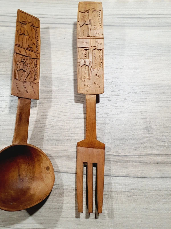 Ensemble de couverts à salade vintage en bois véritable sculpté à la main des années 1970 composé d'une grande fourchette trident et d'une cuillère louche, ornées de motifs de cerfs, biches et faons en relief sur le manche avec encoche repose-plat au dos, montrant un léger éclat de cuisson ou d'usage sur le rebord supérieur du buvant.