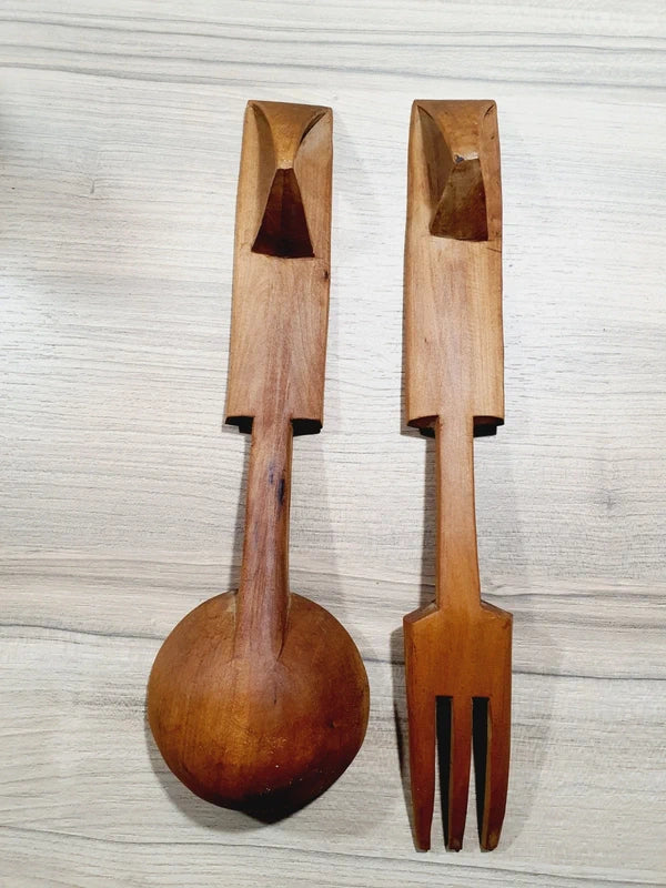 Ensemble de couverts à salade vintage en bois véritable sculpté à la main des années 1970 composé d'une grande fourchette trident et d'une cuillère louche, ornées de motifs de cerfs, biches et faons en relief sur le manche avec encoche repose-plat au dos, montrant un léger éclat de cuisson ou d'usage sur le rebord supérieur du buvant.