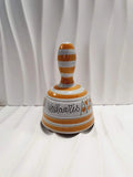 Cloche de table vintage à main en céramique de Vallauris des années 1970 avec des décors graphiques de rayures jaune et orangé sur fond écru, portant l'inscription signature Vallauris peinte à la main au dos et montrant son battant intérieur d'origine.
