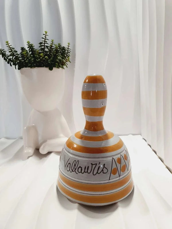 Cloche de table vintage à main en céramique de Vallauris des années 1970 avec des décors graphiques de rayures jaune et orangé sur fond écru, portant l'inscription signature Vallauris peinte à la main au dos et montrant son battant intérieur d'origine.