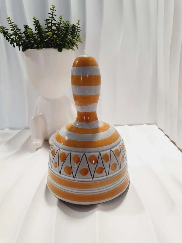 Cloche de table vintage à main en céramique de Vallauris des années 1970 avec des décors graphiques de rayures jaune et orangé sur fond écru, portant l'inscription signature Vallauris peinte à la main au dos et montrant son battant intérieur d'origine.