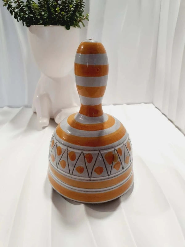 Cloche de table vintage à main en céramique de Vallauris des années 1970 avec des décors graphiques de rayures jaune et orangé sur fond écru, portant l'inscription signature Vallauris peinte à la main au dos et montrant son battant intérieur d'origine.