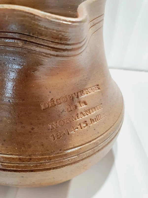 Pichet artisanal en grès véritable brun et beige flammé des années 1970 avec une anse et un bec verseur, affichant une inscription vintage estampée dans la terre Découverte de la Normandie 13-14-15 juillet, montré sous tous les angles avec l'intérieur et sa base propre.