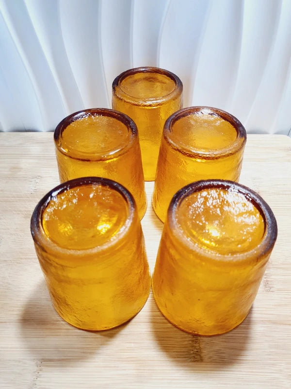 Lot de cinq verres gobelets et photophores vintage des années 1970 en verre épais teinté ambré transparent, avec une texture extérieure givrée effet écorce, style déco bohème chic.