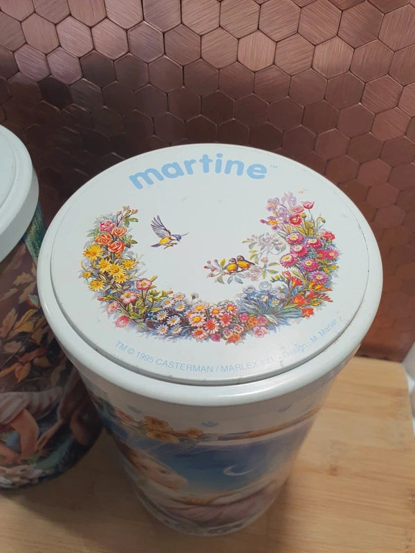 Lot de deux anciennes boîtes à biscuits cylindriques en métal lithographié de l'univers de l'héroïne de livres Martine, illustrations de Marcel Marlier datant des années 1990, parfaites pour le rangement décoratif de la chambre d'enfant.