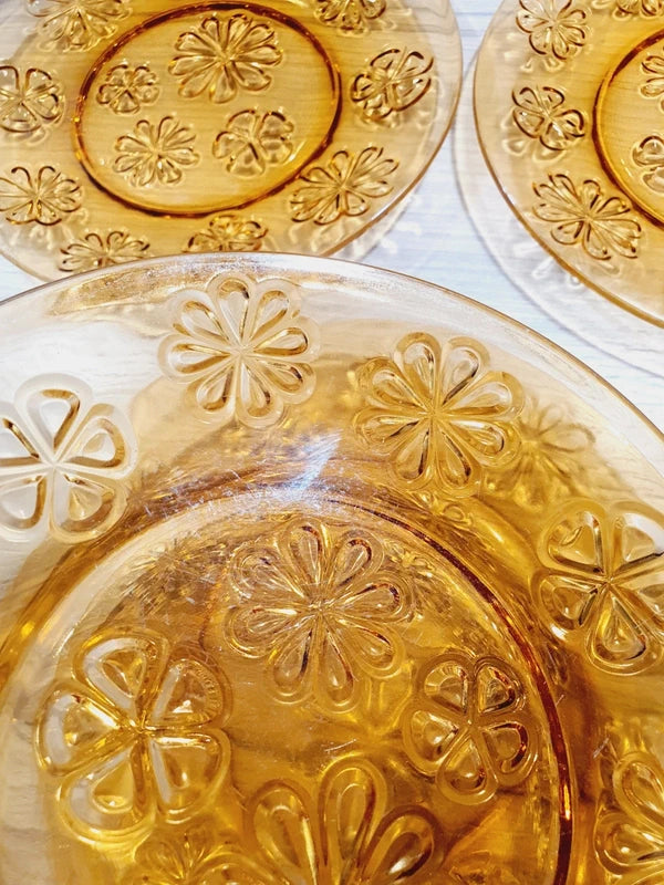 Lot de six assiettes plates rondes à dessert en verre trempé épais de couleur ambrée transparente, ornées d'un motif de fleurs marguerites moulé en relief sur l'extérieur, de la marque française Vereco époque années 1970.
