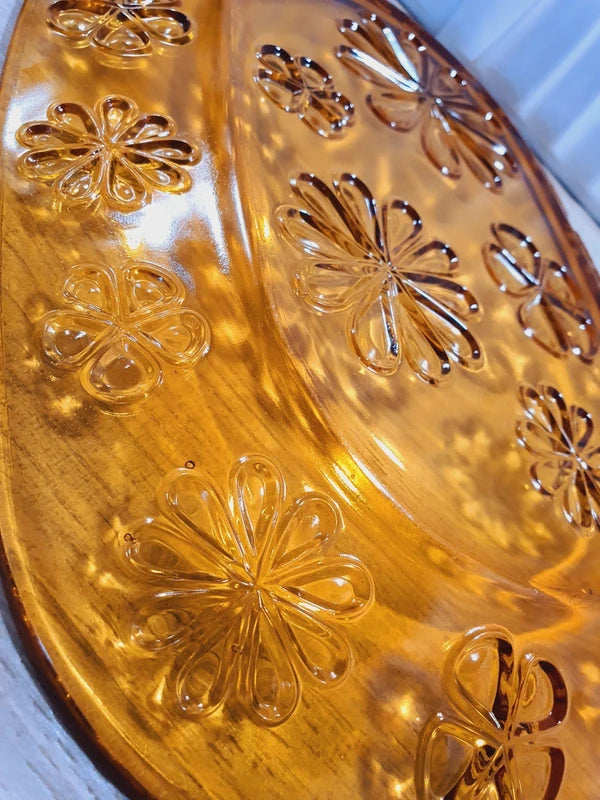 Grand plat de service de forme ovale en verre trempé épais couleur ambre transparent, orné d'un motif de fleurs marguerites moulé en relief sur le dessous, marque Vereco France époque années 1970.