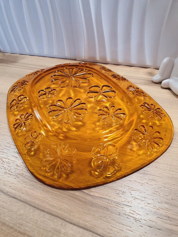 Grand plat de service de forme ovale en verre trempé épais couleur ambre transparent, orné d'un motif de fleurs marguerites moulé en relief sur le dessous, marque Vereco France époque années 1970.