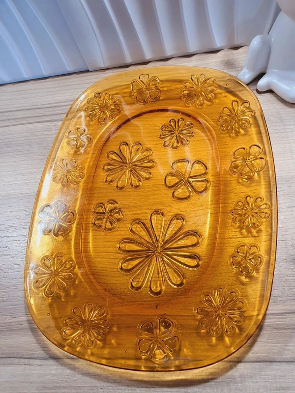 Grand plat de service de forme ovale en verre trempé épais couleur ambre transparent, orné d'un motif de fleurs marguerites moulé en relief sur le dessous, marque Vereco France époque années 1970.