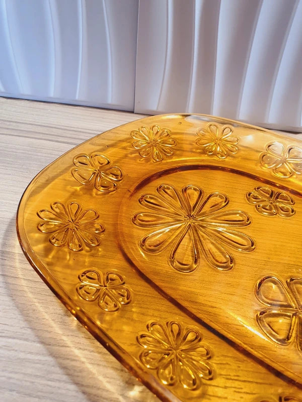 Grand plat de service de forme ovale en verre trempé épais couleur ambre transparent, orné d'un motif de fleurs marguerites moulé en relief sur le dessous, marque Vereco France époque années 1970.